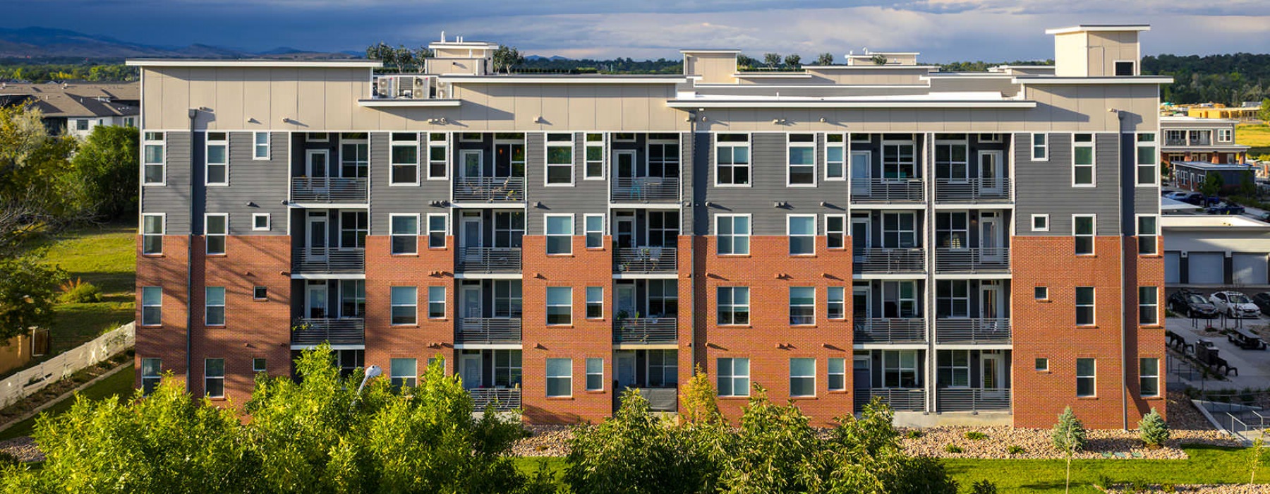 Exterior view of a modern mid-rise apartment building with balconies and landscaped surroundings.