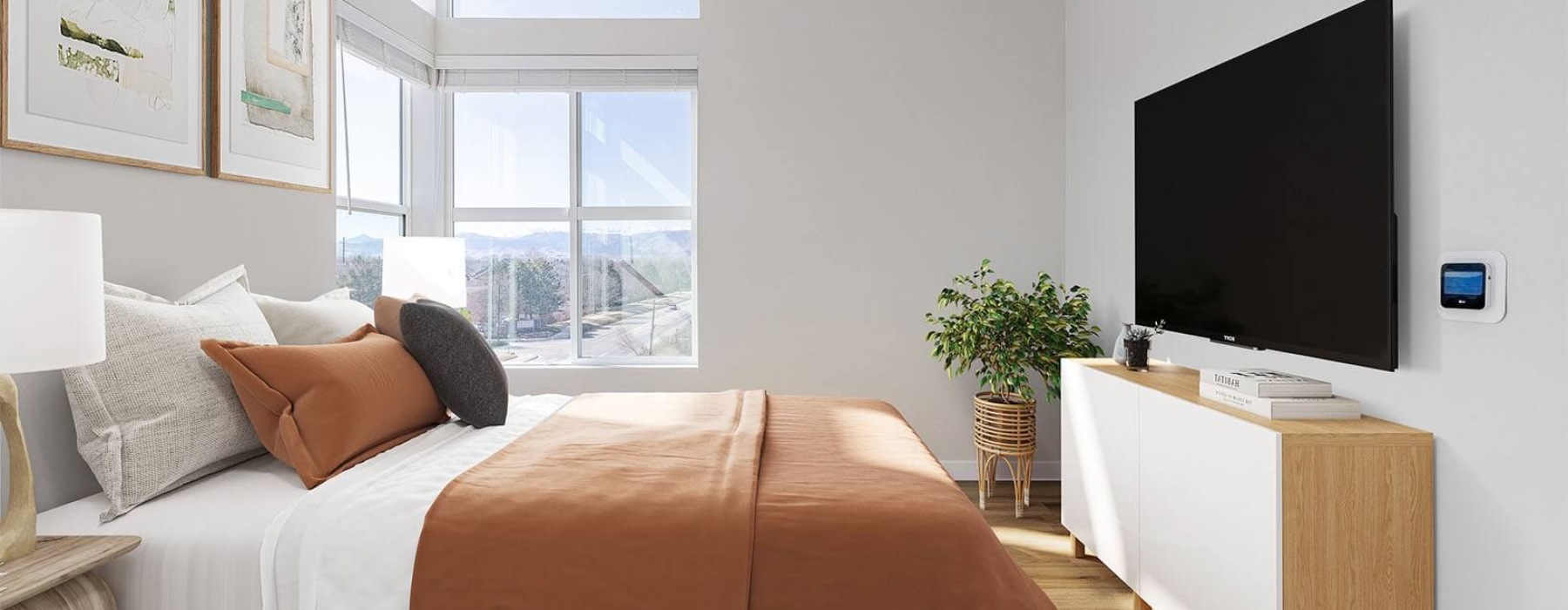 Bright bedroom with large windows, a cozy bed with rust-colored bedding, a wall-mounted TV, and a wooden dresser with a potted plant.